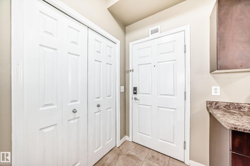 Entryway featuring tile flooring, white paneled doors, and a built-in countertop with dark cabinetry - 411 6925 199 Street Nw, Edmonton, AB - Indoor Photo Showing Other Room