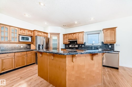 Kitchen featuring a kitchen breakfast bar, light wood-type flooring, a kitchen island, dark stone countertops, and recessed lighting - 1605 Haswell Court, Edmonton, AB - Indoor Photo Showing Kitchen