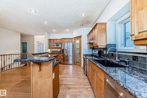Kitchen with stainless steel appliances, a kitchen island, light wood-style floors, a kitchen bar, and decorative backsplash - 1605 Haswell Court, Edmonton, AB - Indoor Photo Showing Kitchen With Upgraded Kitchen