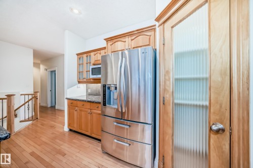Kitchen featuring stainless steel refrigerator with ice dispenser, glass fronted cabinets, light wood-style flooring, white microwave, and dark stone counters - 1605 Haswell Court, Edmonton, AB - Indoor Photo Showing Kitchen
