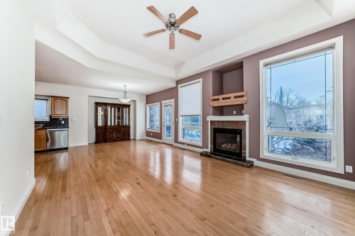 Unfurnished living room with ceiling fan, a raised ceiling, light wood-style floors, and a fireplace - 1605 Haswell Court, Edmonton, AB - Indoor Photo Showing Living Room With Fireplace