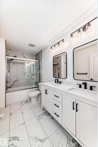 Full bath with double vanity, light marble finish floors, bath / shower combo with glass door, and a textured ceiling - 4008 37 Avenue, Edmonton, AB -  Photo Showing Bathroom