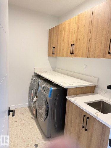 Laundry area featuring light wood-finish cabinetry with matte black hardware, white countertops, and a built-in sink - 53 Lilac Bay, Spruce Grove, AB - Indoor Photo Showing Laundry Room