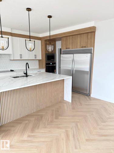 Contemporary kitchen featuring a large island with slatted wood-finish paneling and a quartz countertop - 53 Lilac Bay, Spruce Grove, AB - Indoor Photo Showing Kitchen