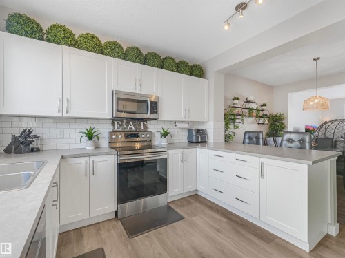 The kitchen features white cabinetry, stainless steel appliances including a microwave and range, light-colored countertops, and a white subway tile backsplash - 725 36 Street, Edmonton, AB - Indoor Photo Showing Kitchen With Double Sink