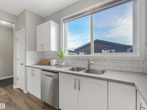 The kitchen features white cabinetry with brushed nickel hardware, a subway tile backsplash, and a double basin stainless steel sink - 725 36 Street, Edmonton, AB - Indoor Photo Showing Kitchen With Double Sink