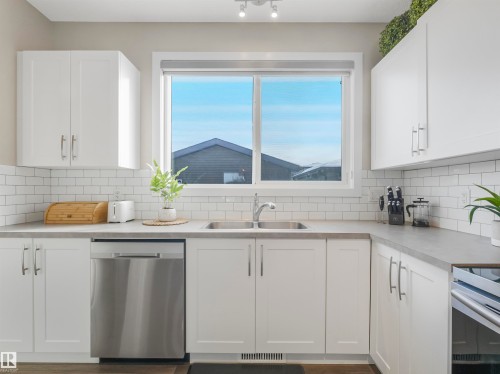 The kitchen features white cabinetry, a double basin sink, and a stainless steel dishwasher - 725 36 Street, Edmonton, AB - Indoor Photo Showing Kitchen With Double Sink