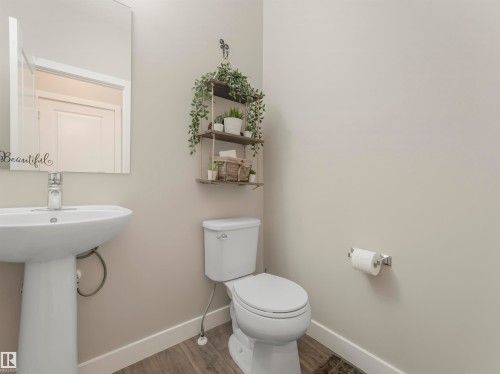 Bathroom featuring a pedestal sink, a toilet, a wall-mounted mirror, and wood-look flooring - 725 36 Street, Edmonton, AB - Indoor Photo Showing Bathroom