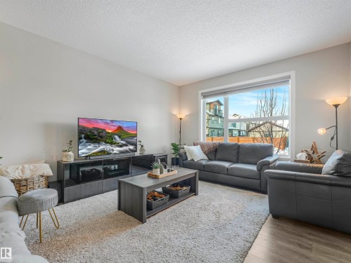 The living area features a large window providing natural light, light-toned walls, and a textured carpet - 725 36 Street, Edmonton, AB - Indoor Photo Showing Living Room