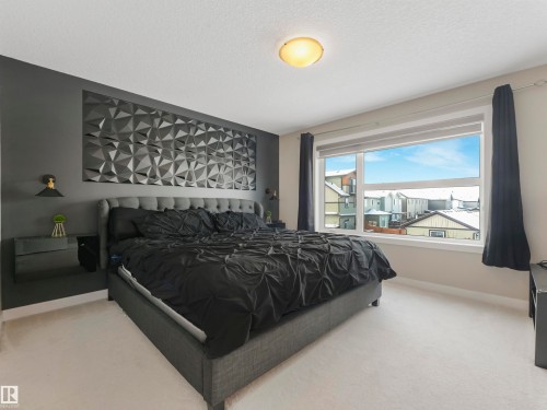 Bedroom featuring a textured accent wall, a wide window with dark curtains, and light-colored carpeting - 725 36 Street, Edmonton, AB - Indoor Photo Showing Bedroom