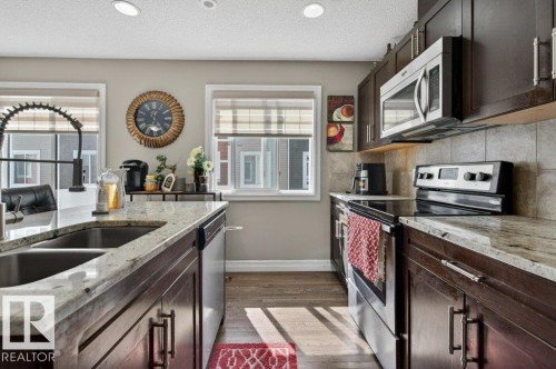 Modern kitchen featuring dark wood cabinetry, light-toned countertops, and stainless steel appliances - 40 14621 121 Street, Edmonton, AB - Indoor Photo Showing Kitchen With Double Sink