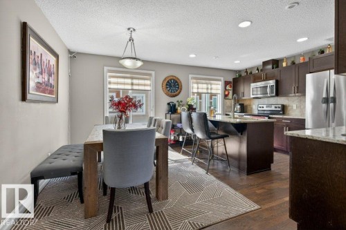 Open-concept kitchen and dining area featuring dark wood-finish cabinetry, stainless steel appliances, a center island with bar seating, and recessed lighting - 40 14621 121 Street, Edmonton, AB - Indoor