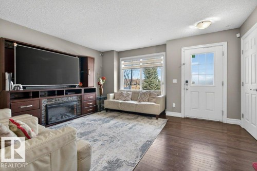 Living room featuring a built-in entertainment center with an electric fireplace, wood-finish flooring, and a large window with blinds - 40 14621 121 Street, Edmonton, AB - Indoor Photo Showing Living Room With Fireplace