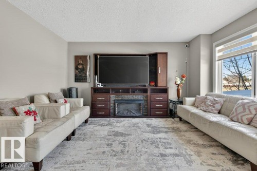 Living area featuring a built-in entertainment unit with integrated fireplace, neutral wall tones, and a large window with roller shades - 40 14621 121 Street, Edmonton, AB - Indoor Photo Showing Living Room