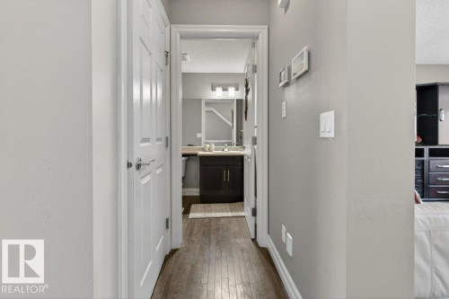 Hallway with wood-finish flooring leading to a bathroom featuring a dark wood vanity, light-toned countertop, and modern lighting fixture - 40 14621 121 Street, Edmonton, AB - Indoor Photo Showing Other Room