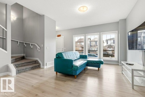 Bright living area featuring light wood-finish flooring, three large windows, a textured ceiling, and a carpeted staircase with a white railing - 17451 77 Street, Edmonton, AB - Indoor Photo Showing Living Room