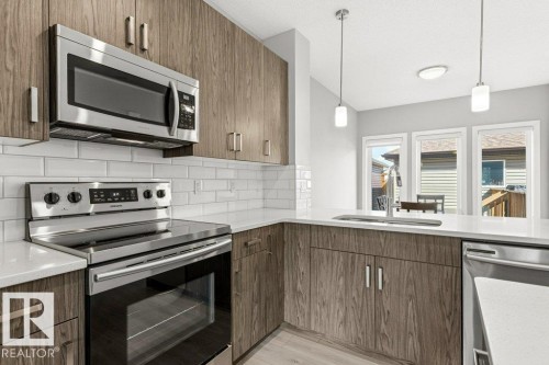 Kitchen featuring wood-finish cabinetry, stainless steel appliances, white subway tile backsplash, light-toned countertops, and multiple windows - 17451 77 Street, Edmonton, AB - Indoor Photo Showing Kitchen With Upgraded Kitchen