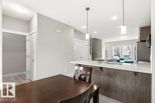 Modern kitchen featuring a large island with white countertops, integrated sink, stainless steel appliances, and two pendant lights - 17451 77 Street, Edmonton, AB - Indoor Photo Showing Other Room