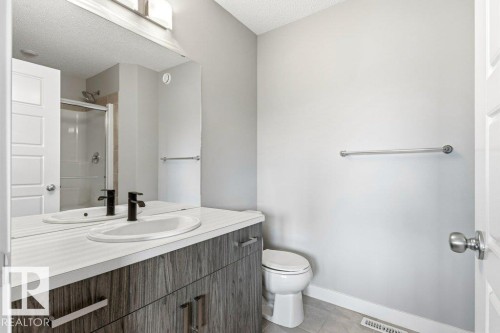 Bathroom featuring a wood-grain vanity with a white countertop and integrated sink, matte black faucet, and a large mirror - 17451 77 Street, Edmonton, AB - Indoor Photo Showing Bathroom