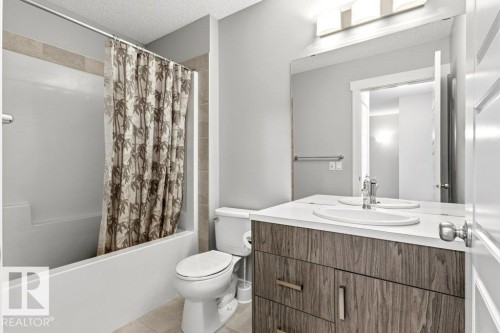 Bathroom featuring a built-in tub with tile surround, wood-finish vanity with an integrated sink, polished chrome faucet, and overhead lighting fixture - 17451 77 Street, Edmonton, AB - Indoor Photo Showing Bathroom