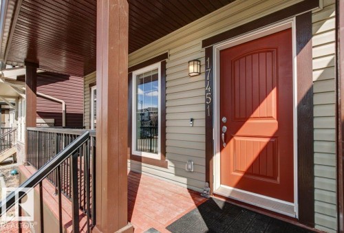 Covered front porch featuring a paneled entry door, vertical siding, a rectangular window with white trim, and a black metal railing - 17451 77 Street, Edmonton, AB - Outdoor With Exterior