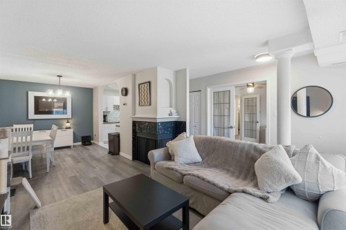 Living space featuring wood-finish flooring, a decorative fireplace with dark tile surround, and an arched entry - 5740 172 Street, Edmonton, AB - Indoor Photo Showing Living Room