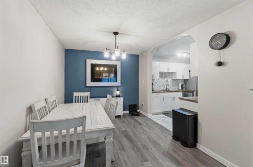 Dining area featuring wood-finish flooring, a contemporary chandelier, and an accent wall with a wall-mounted electric fireplace - 5740 172 Street, Edmonton, AB - Indoor Photo Showing Dining Room