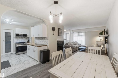 Open-concept living area featuring a kitchen with stainless steel appliances, white cabinetry, and a herringbone-patterned backsplash - 5740 172 Street, Edmonton, AB - Indoor