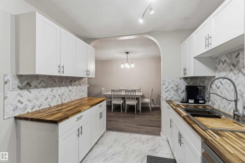 Contemporary kitchen featuring white cabinetry, wood-finish countertops, a herringbone tile backsplash, and stainless steel sink with a gooseneck faucet - 5740 172 Street, Edmonton, AB - Indoor Photo Showing Kitchen With Double Sink