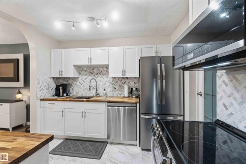 Kitchen featuring white cabinetry, wood-finish countertops, herringbone tile backsplash, stainless steel appliances, and track lighting - 5740 172 Street, Edmonton, AB - Indoor Photo Showing Kitchen