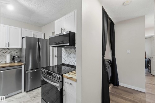 Modern kitchen featuring stainless steel appliances, white cabinetry, wood-finish countertops, and a herringbone tile backsplash - 5740 172 Street, Edmonton, AB - Indoor Photo Showing Kitchen