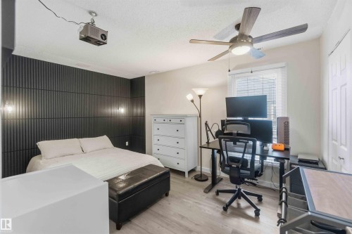 Bedroom featuring a dark accent wall with vertical paneling, two wall-mounted sconces, and wood-finish flooring - 5740 172 Street, Edmonton, AB - Indoor