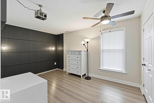 Accent wall with vertical slat detailing, integrated sconce lighting, and wood-finish flooring - 5740 172 Street, Edmonton, AB - Indoor