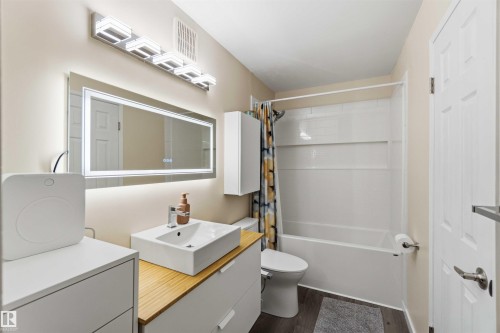 Bathroom featuring a white rectangular vessel sink, wood-finish countertop, white cabinetry with silver hardware, an illuminated mirror, and a full bathtub with white subway tile surround - 5740 172 Street, Edmonton, AB - Indoor Photo Showing Other Room