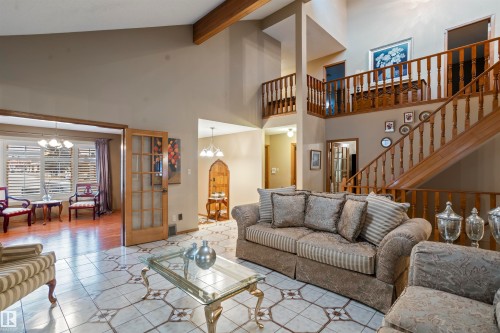 Spacious living area featuring a two-story ceiling, a grand wooden staircase, patterned tile flooring, and exposed wooden beams - 9831 158 Avenue, Edmonton, AB - Indoor Photo Showing Living Room
