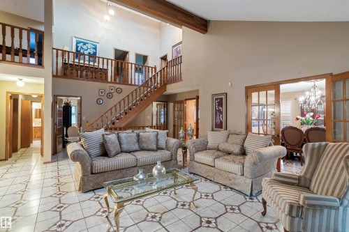 Spacious living area featuring patterned tile flooring, exposed wood beam accents, and a grand wooden staircase with an open-concept upper-level balcony - 9831 158 Avenue, Edmonton, AB - Indoor Photo Showing Living Room
