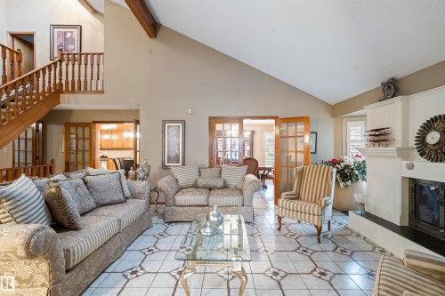 Spacious living area featuring a vaulted ceiling with exposed wood beams, a wood-finish staircase, and patterned tile flooring - 9831 158 Avenue, Edmonton, AB - Indoor Photo Showing Living Room With Fireplace