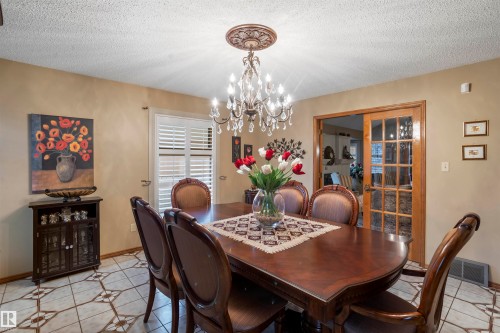 Formal dining area featuring a crystal chandelier with an ornate ceiling medallion, plantation shutters, and wood-frame French doors - 9831 158 Avenue, Edmonton, AB - Indoor Photo Showing Dining Room