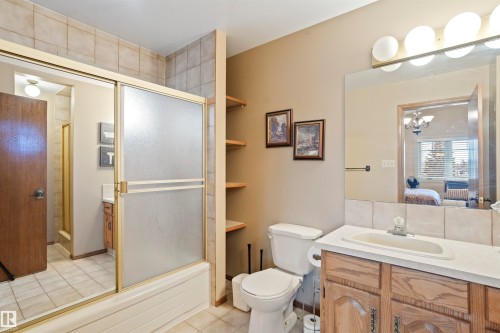 Bathroom featuring a tiled tub and shower combination with sliding frosted glass doors, light wood-finish vanity with an integrated sink, and a rectangular mirror with overhead vanity lighting - 9831 158 Avenue, Edmonton, AB - Indoor Photo Showing Bathroom