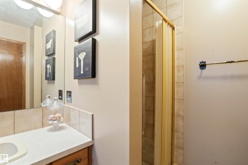 Bathroom featuring a built-in vanity with an integrated sink, a tiled countertop, and a mirrored wall with an overhead light fixture - 9831 158 Avenue, Edmonton, AB - Indoor Photo Showing Bathroom