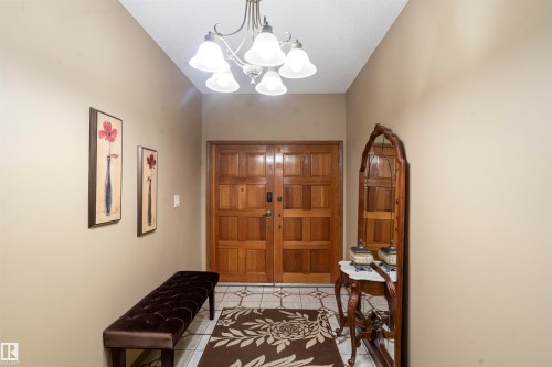 Solid wood double entry doors with decorative panels, overhead chandelier, and light-toned tile flooring - 9831 158 Avenue, Edmonton, AB - Indoor Photo Showing Other Room