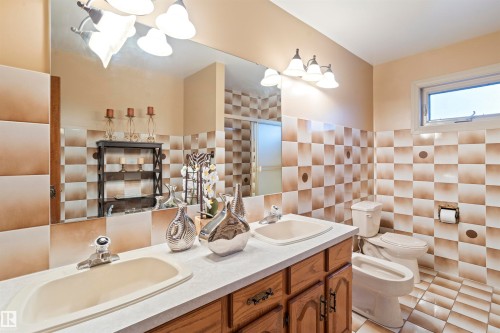 Bathroom featuring a dual vanity with oak cabinetry, checkerboard wall tile, and a window for natural light - 9831 158 Avenue, Edmonton, AB - Indoor Photo Showing Bathroom