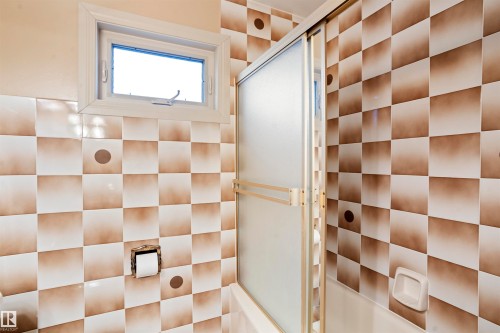 Bathroom featuring checkered wall tiling, a frosted glass shower enclosure, and a window with a cream-colored frame - 9831 158 Avenue, Edmonton, AB - Indoor