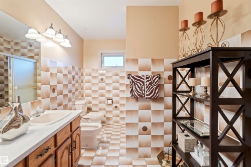 Bathroom featuring checkerboard wall and floor tiles, a single vanity with wood cabinetry and a white countertop, a toilet, a frosted glass shower enclosure, and a built-in shelving unit - 9831 158 Avenue, Edmonton, AB - Indoor