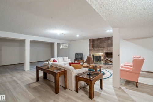 Spacious recreation area featuring light wood-finish flooring, recessed lighting, and a brick fireplace with a brass firebox - 9831 158 Avenue, Edmonton, AB - Indoor With Fireplace