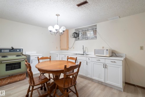 Open-concept kitchen area featuring a built-in oven, white cabinetry, a single basin sink, and wood-finish flooring - 9831 158 Avenue, Edmonton, AB - Indoor