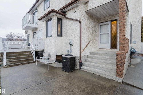 Concrete patio area featuring direct access to the interior, an exterior staircase leading to an upper-level balcony, and a brick-clad architectural element - 9831 158 Avenue, Edmonton, AB - Outdoor With Exterior