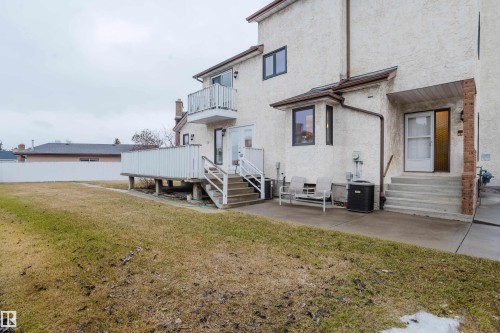 Rear exterior featuring a ground-level patio, a raised deck with stairs, a second-story balcony, and a stucco finish - 9831 158 Avenue, Edmonton, AB - Outdoor