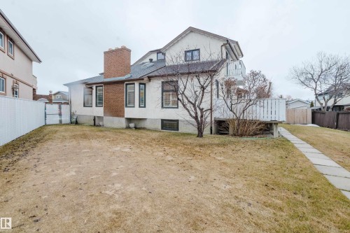 Rear exterior featuring a brick chimney, a white privacy fence, a ground-level deck with white railing, and a stepped concrete pathway - 9831 158 Avenue, Edmonton, AB - Outdoor