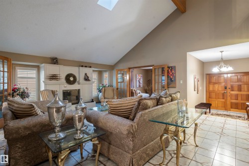Living area featuring vaulted ceilings with exposed wood beams, a central fireplace with a mantel, and patterned tile flooring - 9831 158 Avenue, Edmonton, AB - Indoor Photo Showing Living Room With Fireplace